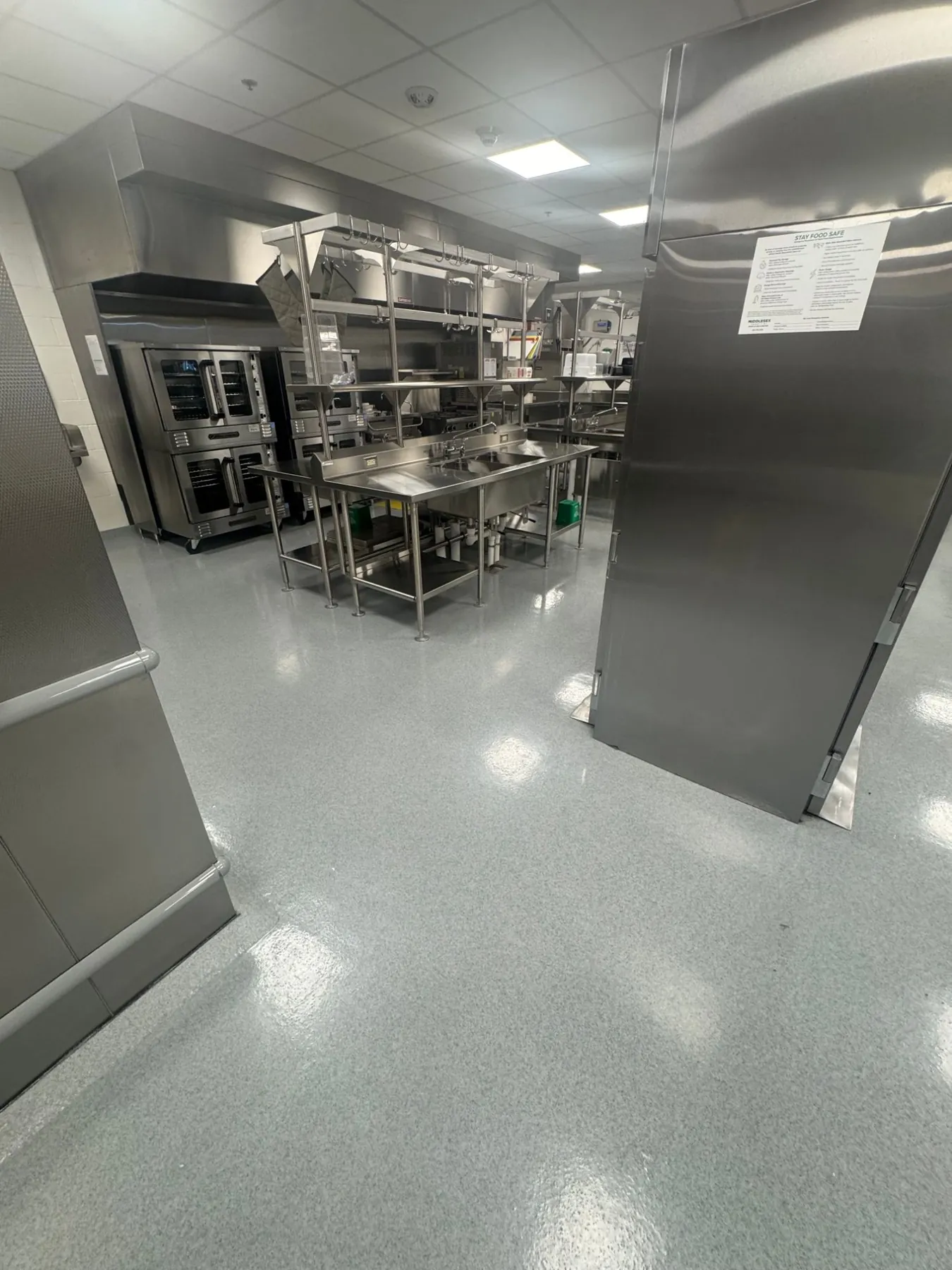 Gray epoxy quartz floor in a college kitchen, running past convection ovens and a prep sink